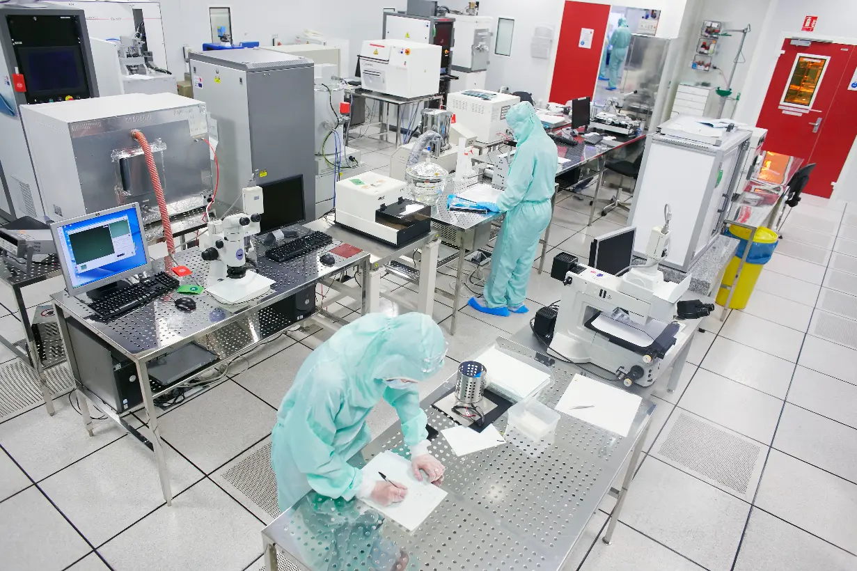 Salle blanche de laboratoire avec des chercheurs en tenue stérile travaillant sur des équipements de pointe pour l’analyse scientifique.
