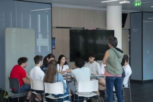 Un groupe d'élève de l'IMT assis autour d'une table en discussion avec leur coach, lors du challenge convergence.