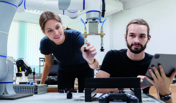 Deux chercheurs collaborant dans un laboratoire de robotique, manipulant des composants et utilisant une tablette pour les contrôles.