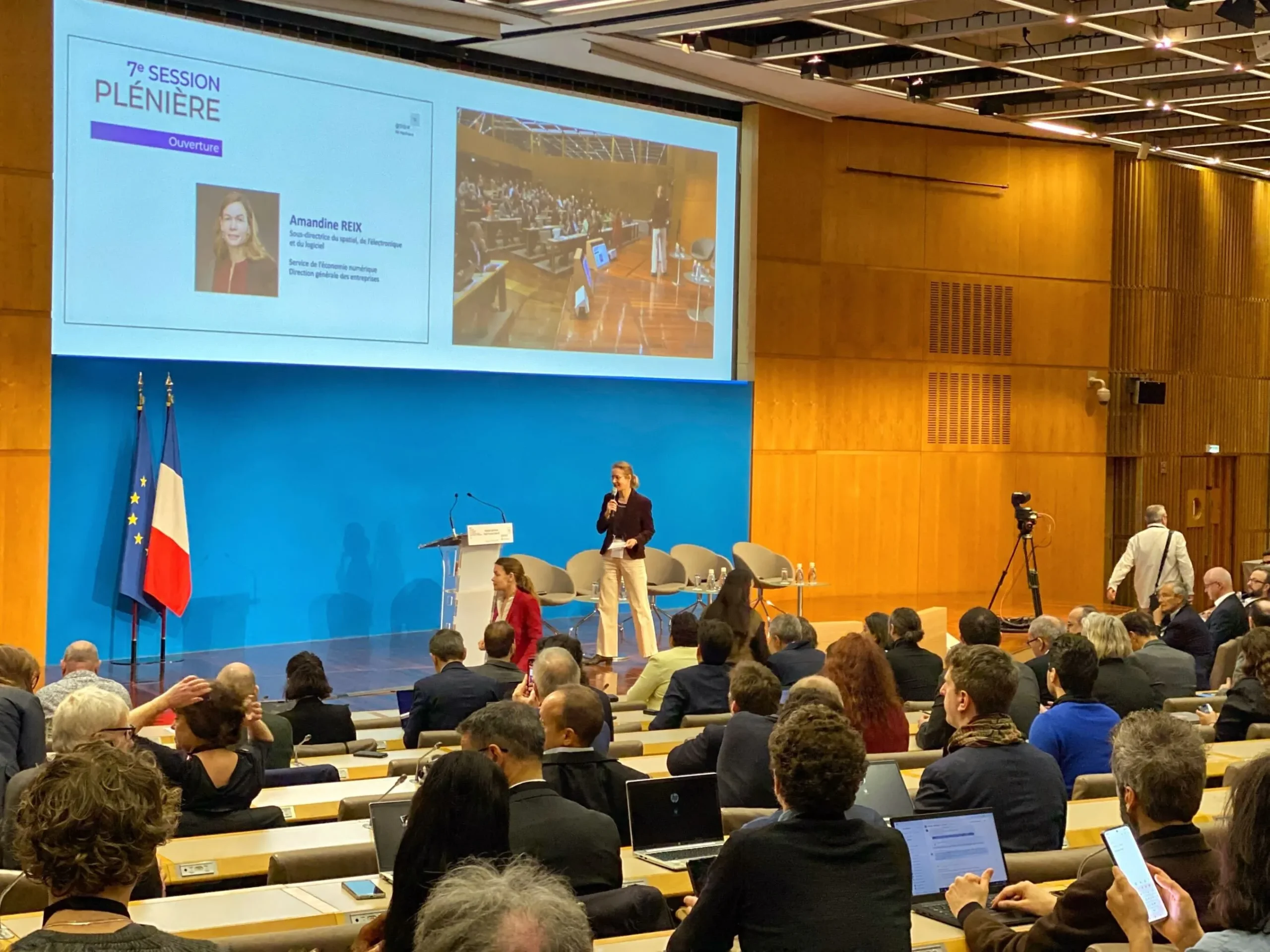 Vue de la salle lors de la 7ᵉ session plénière du Hub France Gaia-X, le 6 mars 2025 à Bercy. À l’écran, la présentation d’Amandine Reix, cheffe du service de l’économie numérique à la DGE. Une intervenante s’exprime sur scène devant un public attentif.